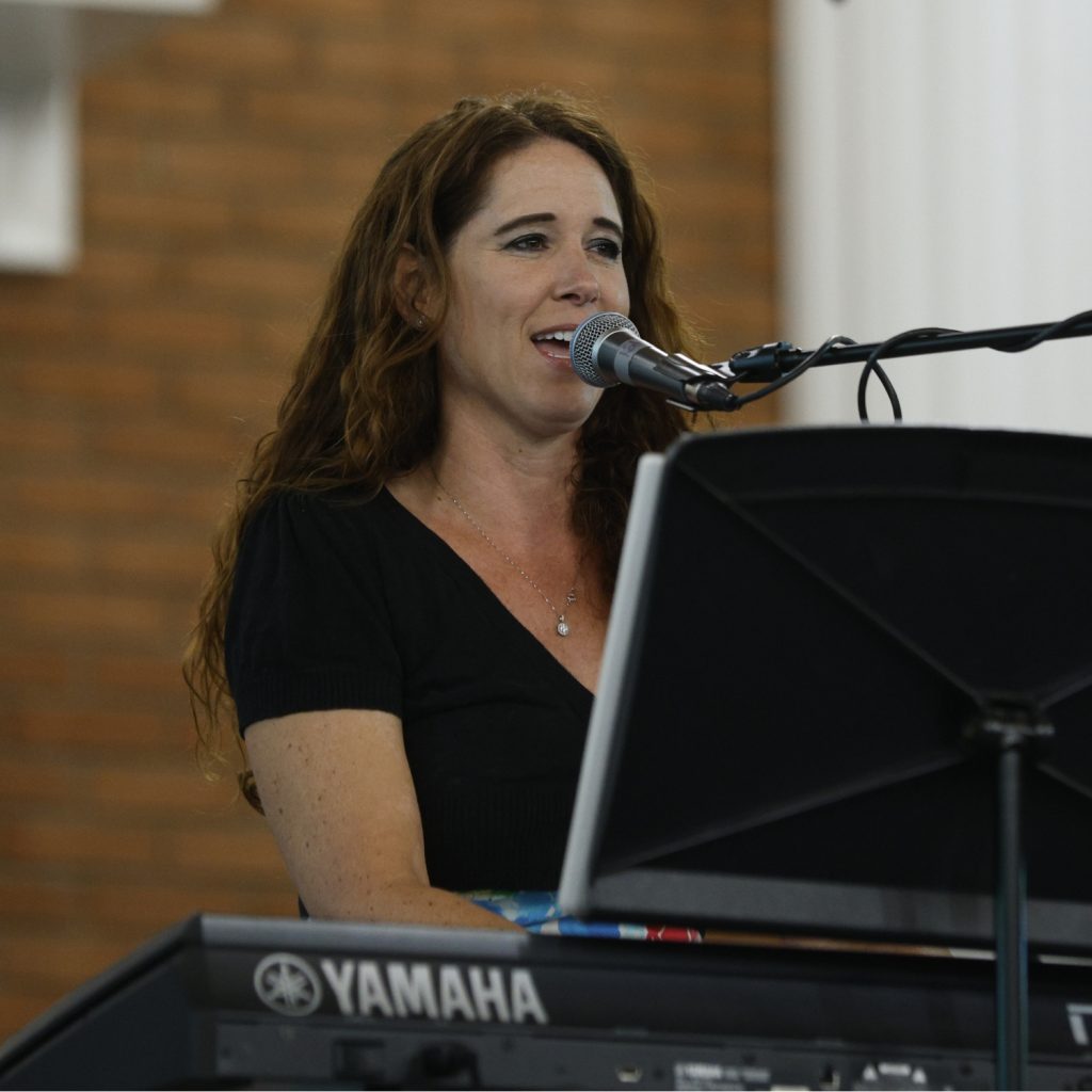 Music Leader singing into a microphone while playing keyboard at Sunday worship service.